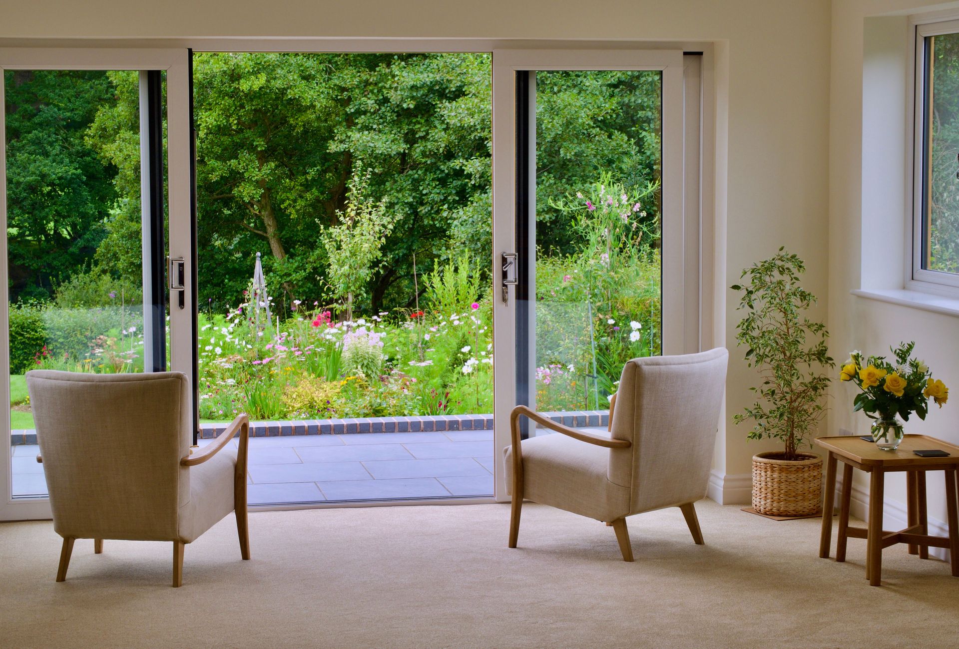 Cozy interior with armchairs and greenery view through large sliding glass doors.